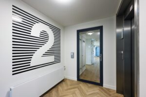 Moderne gang op de tweede verdieping met een lift, glazen deur en opvallend muurontwerp met het cijfer 2.